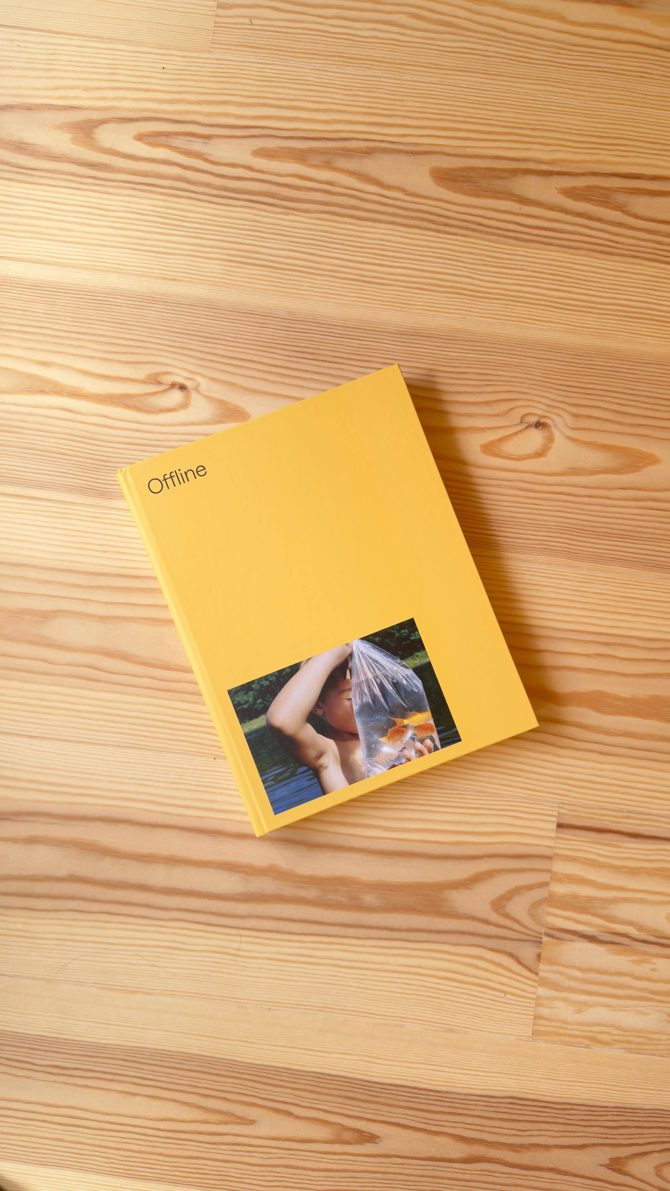 Een FOTOFOTO fotoboek met gele kaft op een houten vloer